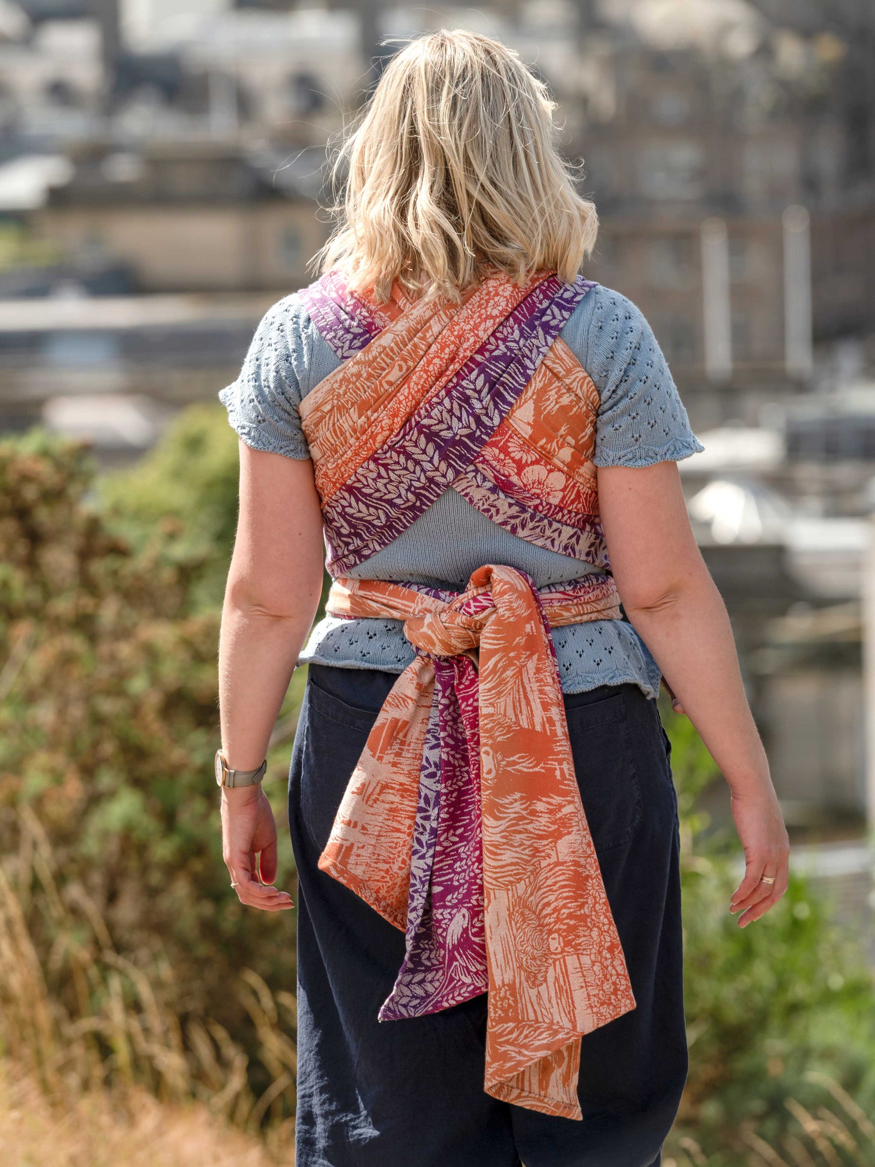 Back of a woman wearing a colurful woven baby wrap.