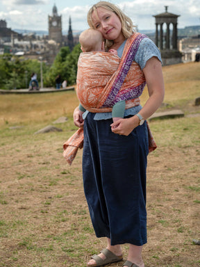 Side view of a a mum carrying a baby in a colourful woven wrap.
