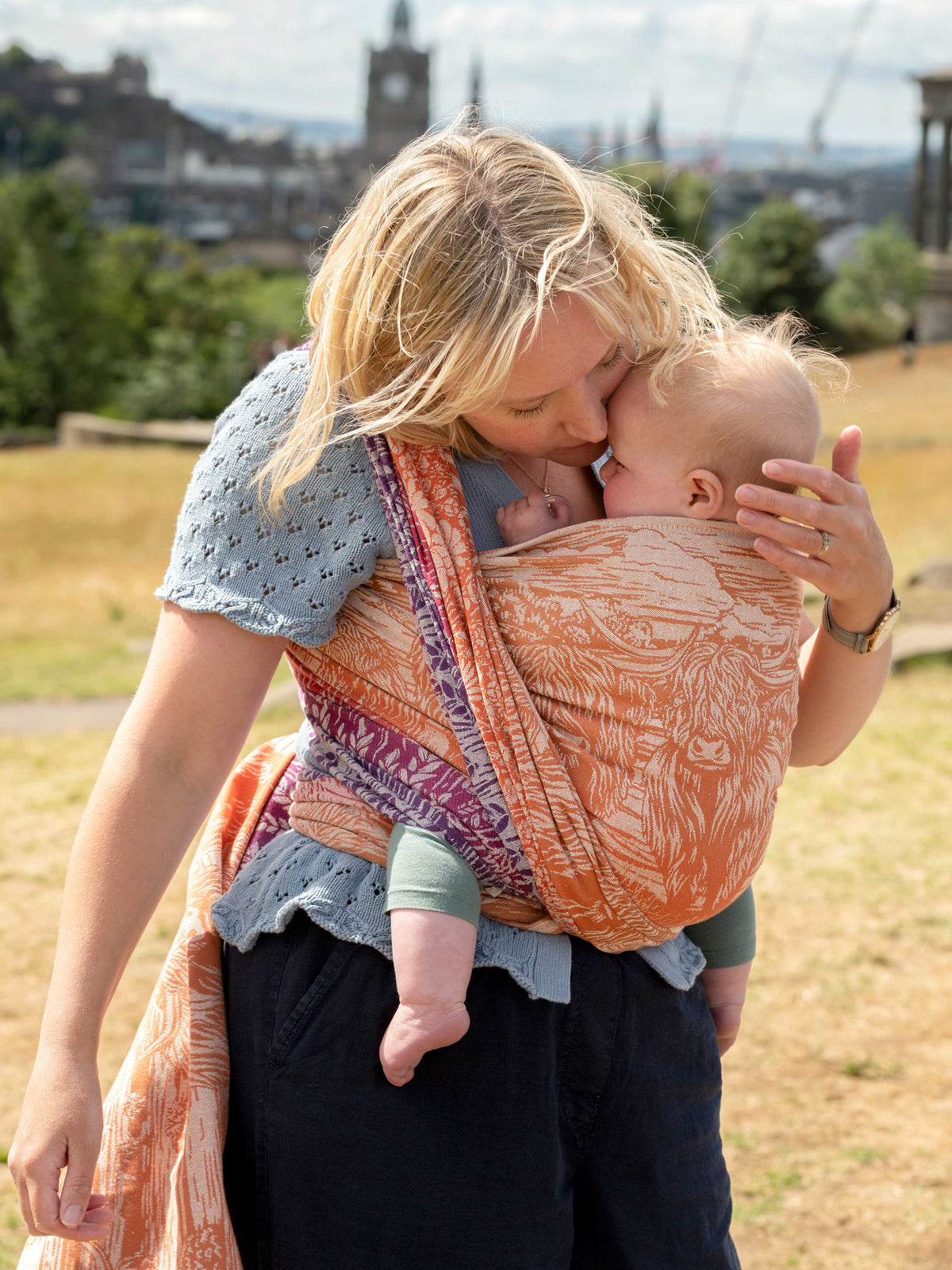 A mum carrying a baby in a colourful woven wrap.
