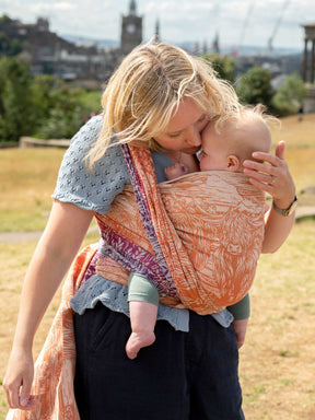 A mum carrying a baby in a colourful woven wrap.