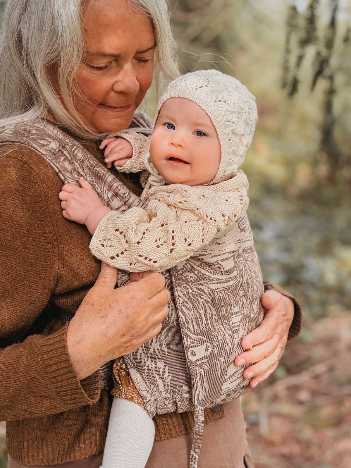 Woman holding a baby in a patterned baby carrier outdoors