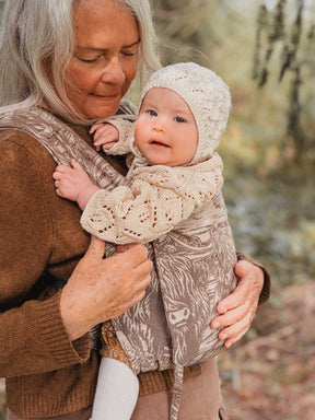 Woman holding a baby in a patterned baby carrier outdoors