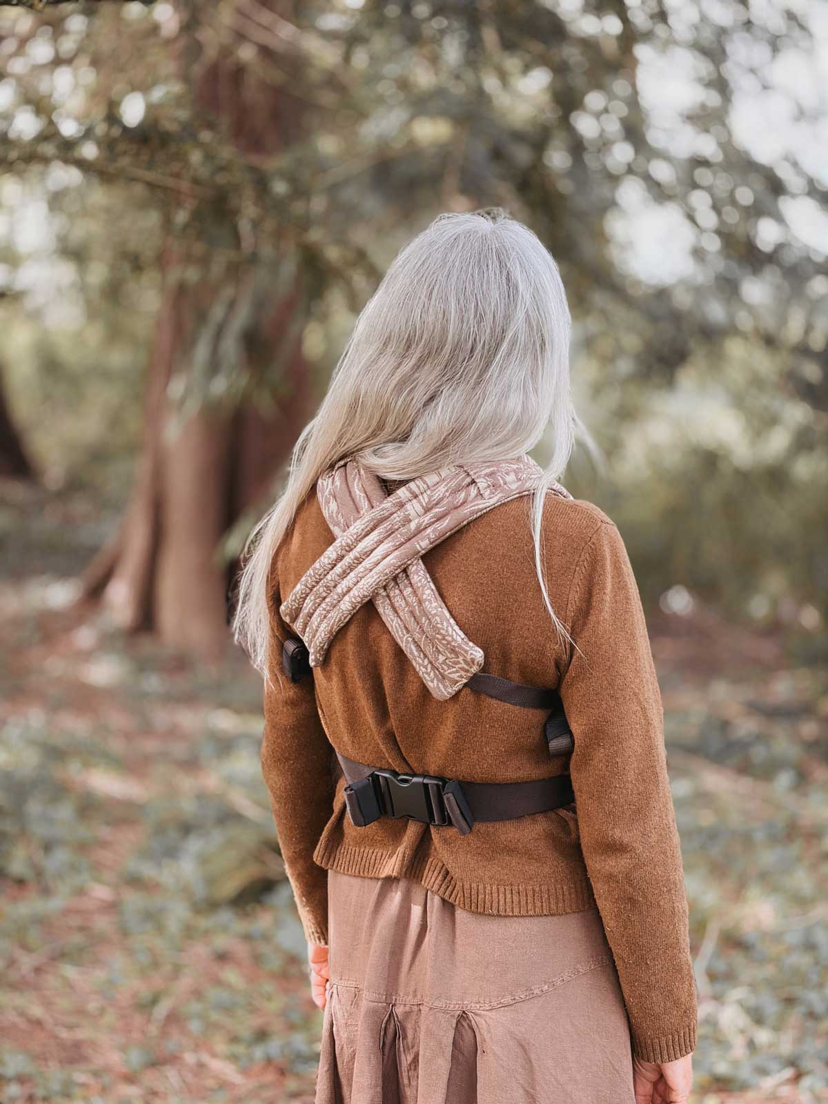 The back of a woman wearing a baby carrier outdoors.
