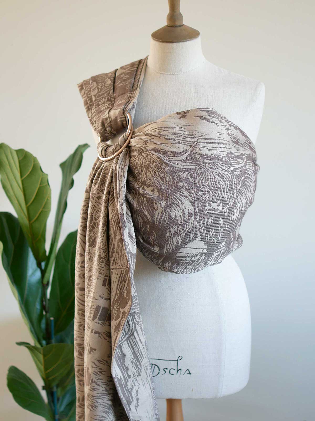 Mannequin wearing a highland cow patterned ring sling with a plant in the background