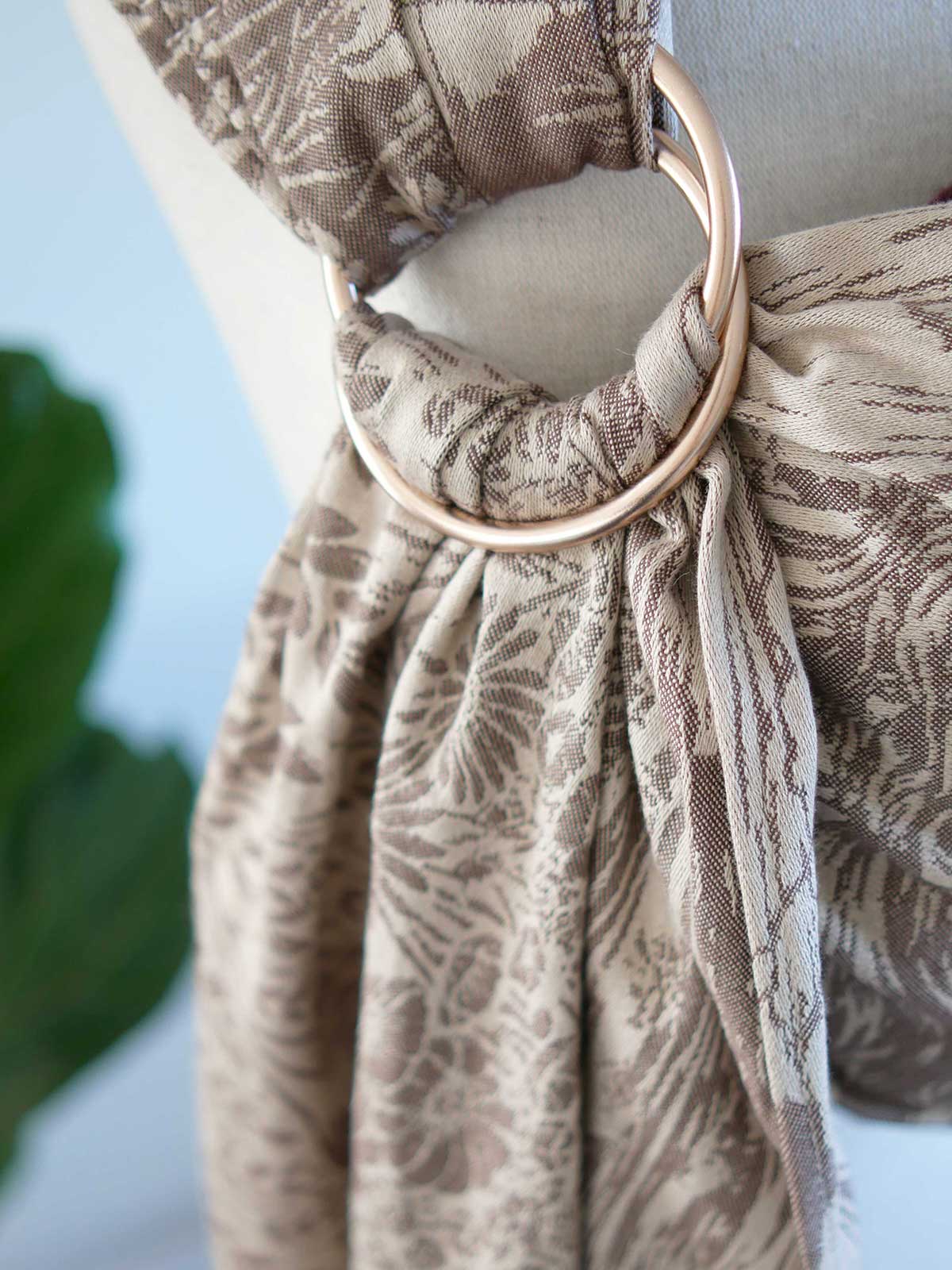 Close-up of a patterned fabric with a champagne ring, against a blurred natural background.