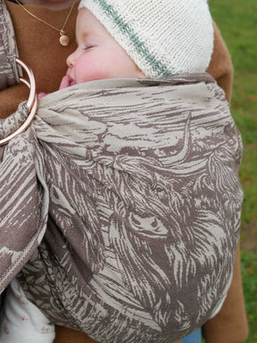 Baby wrapped in a patterned ring sling with a blurred natural background