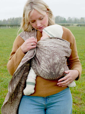 Woman holding a baby in a sling outdoors in a field