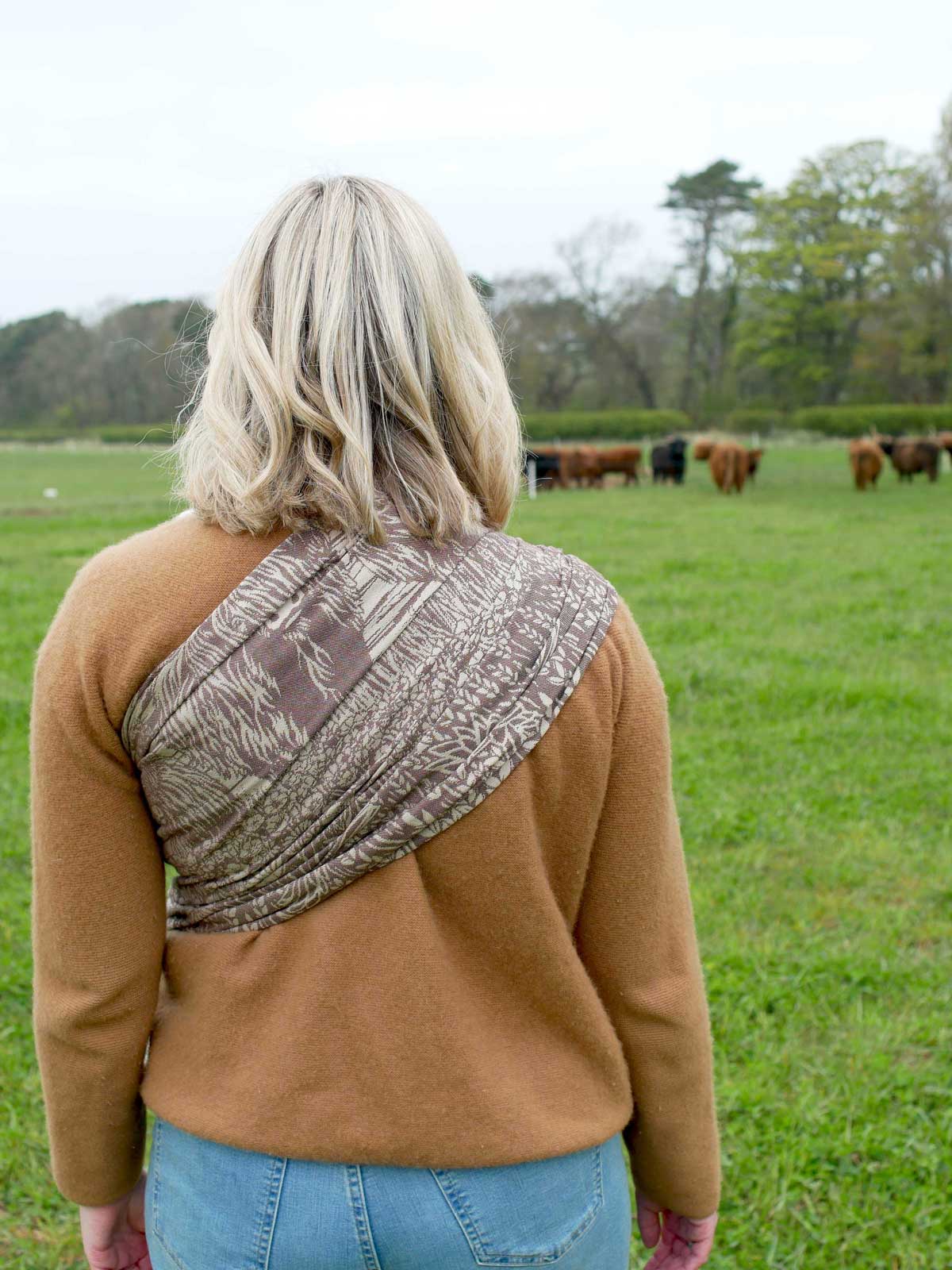 Person wearing a brown jacket with a patterned back in a field with cows.