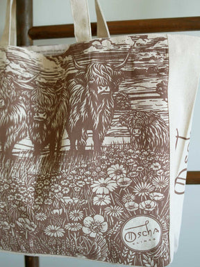Close up of canvas tote bag with highland cow design hanging on a rail