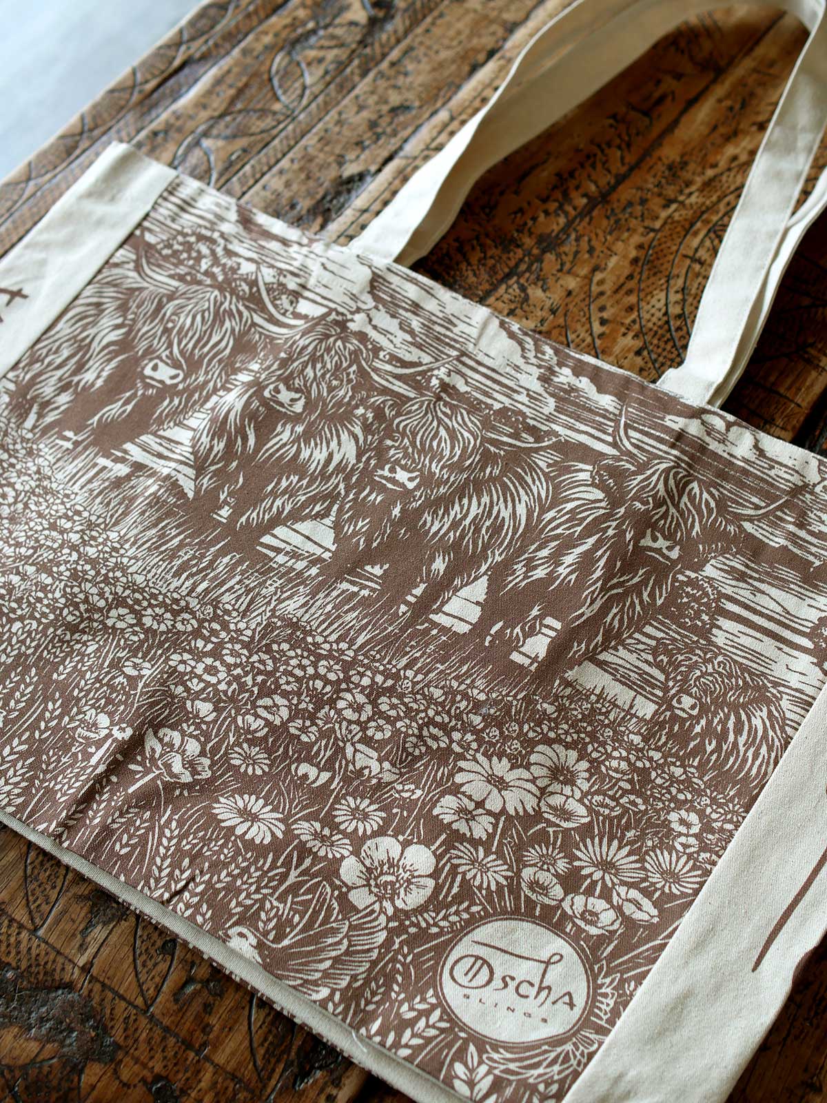 Canvas tote bag with highland cow design lying flat on wooden surface