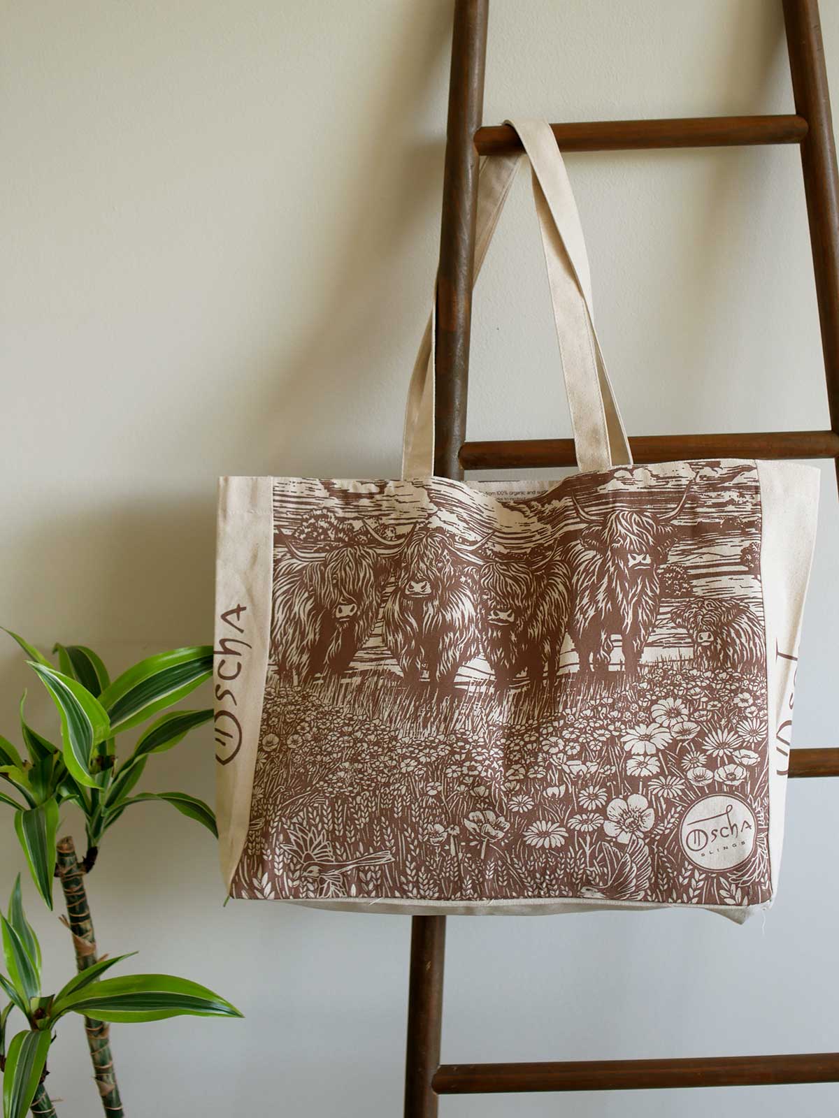 Canvas tote bag with highland cow design hanging on a rail