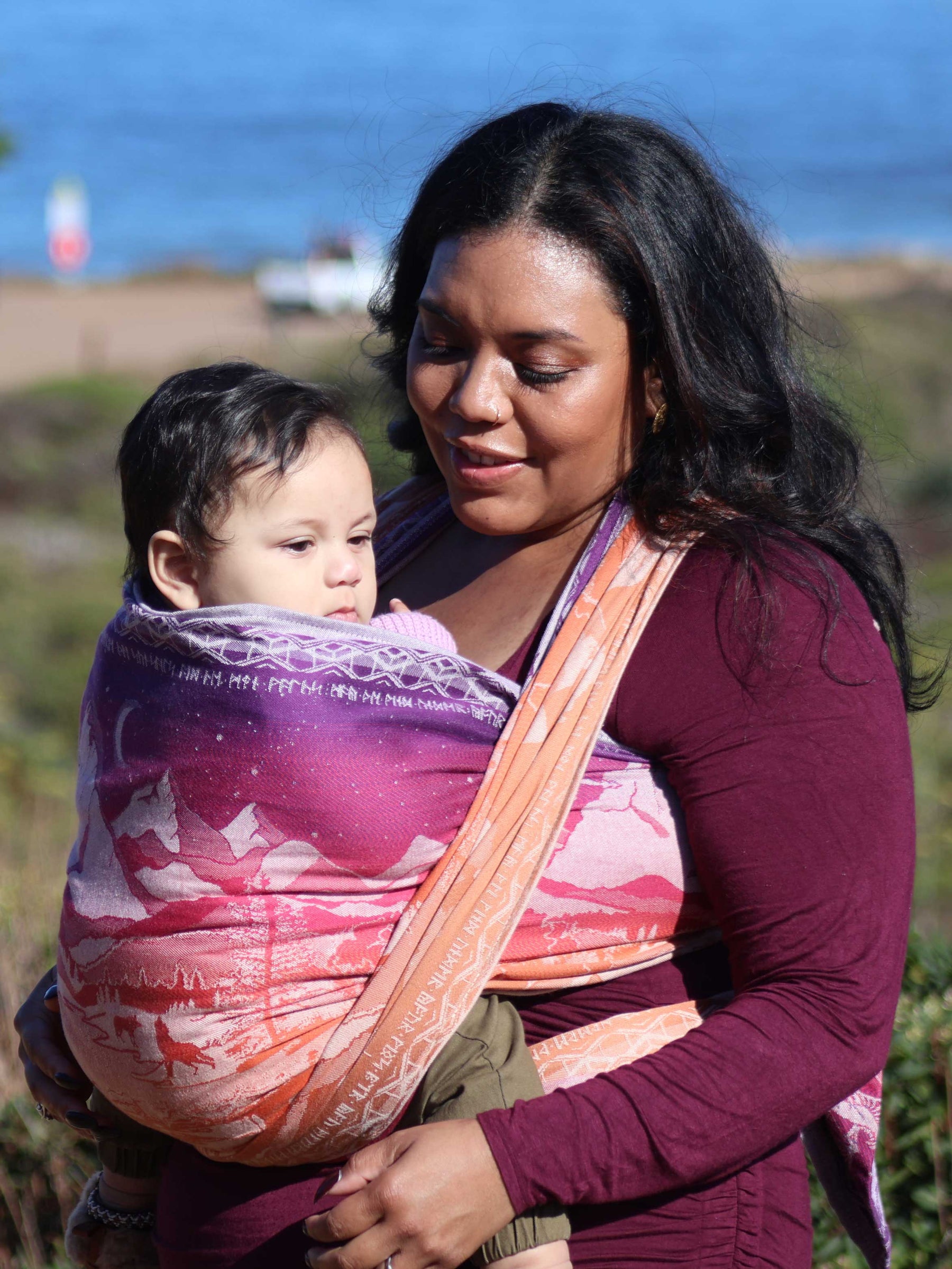 Model smiles at baby son wearing this Hobbit Quest design baby wrap. 