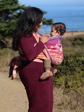 Side view of model wearing baby in a wrap which is glowing with purple, pink and orange. 