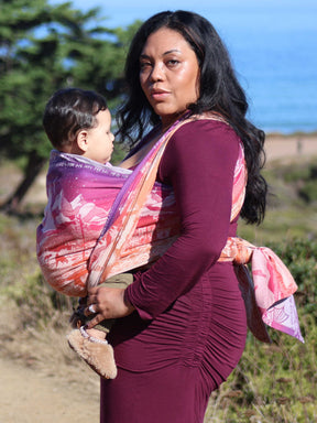 Left side view of model and baby with baby wrap. Ocean view in the background. 