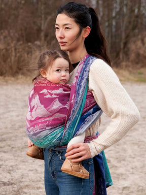 Woman carrying a child in a jewel coloured baby wrap outdoors.