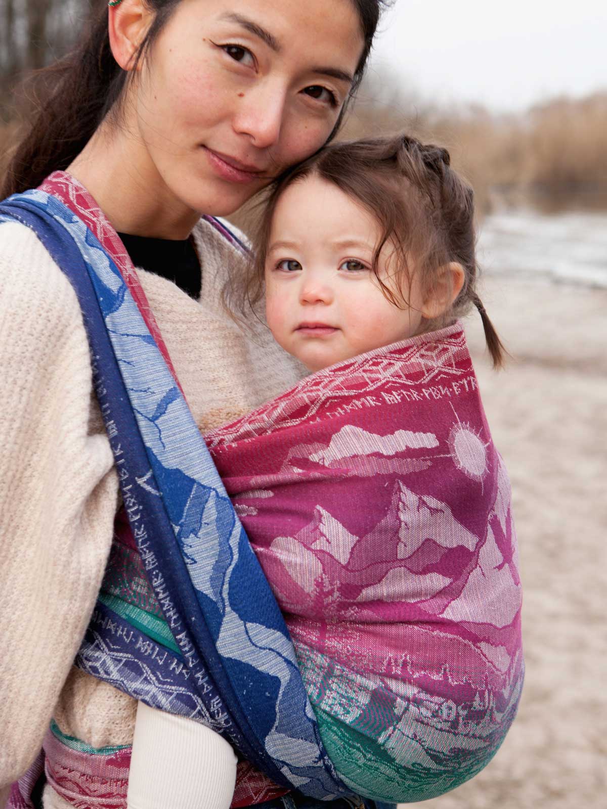 Woman holding a child in a colourful baby wrap outdoors.