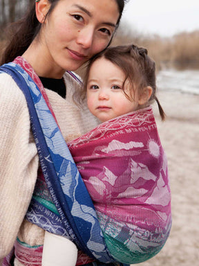 Woman holding a child in a colourful baby wrap outdoors.