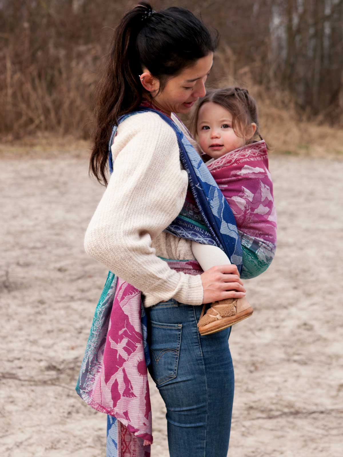 Woman holding a child wrapped in a colourful woven wrap outdoors.