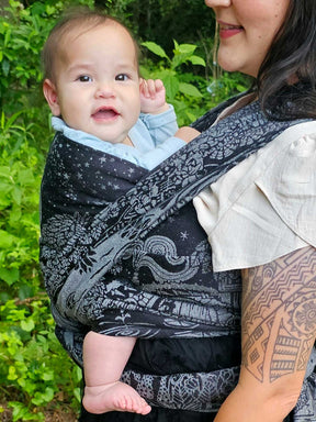 Close up of a baby being carried in a black and silver woven wrap