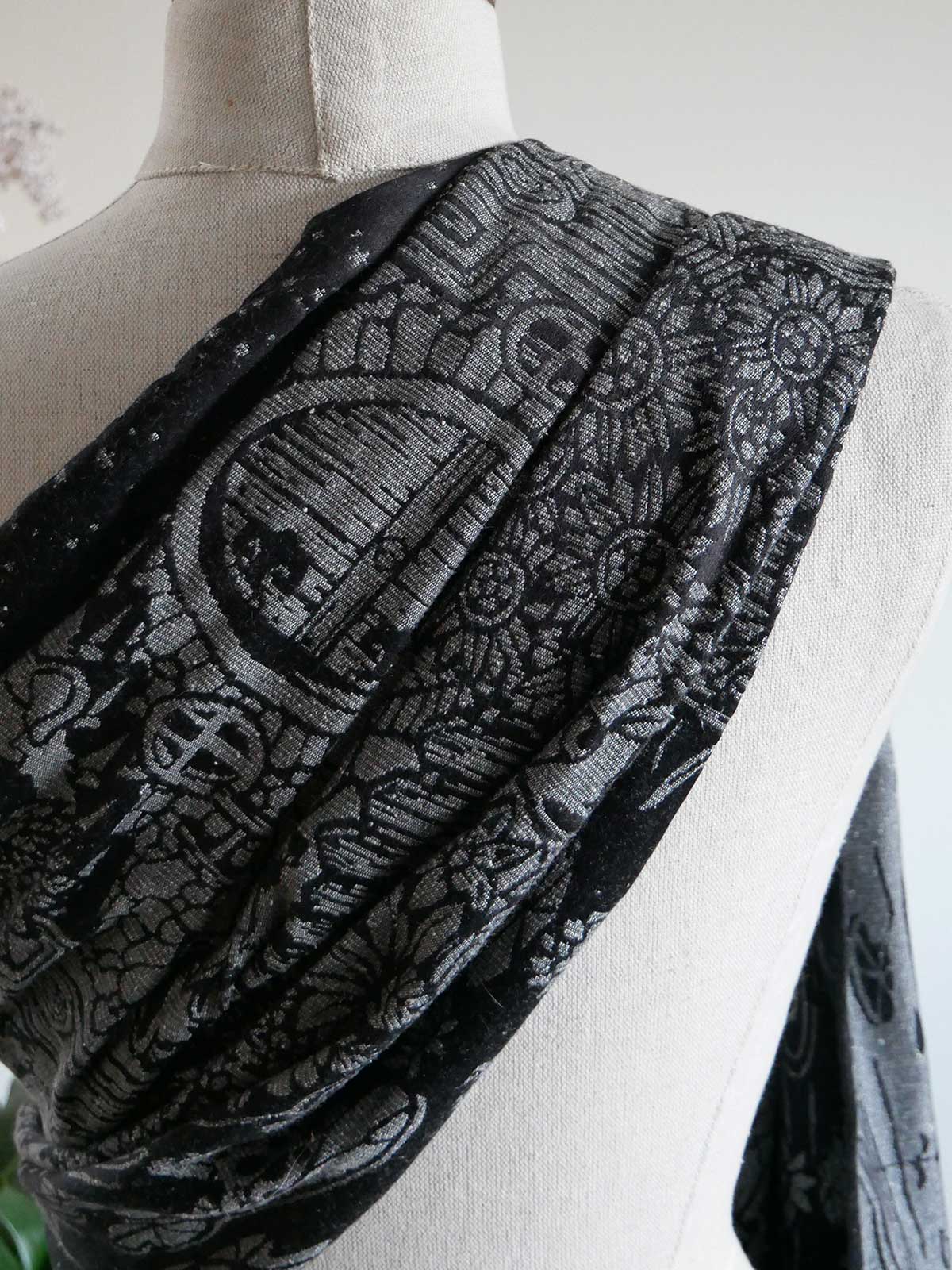 Back of a mannequin with black and grey fabric draped over the shoulder.
