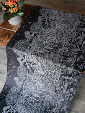 Black fabric with silvery hobbit house and foliage design laid on a wooden table.