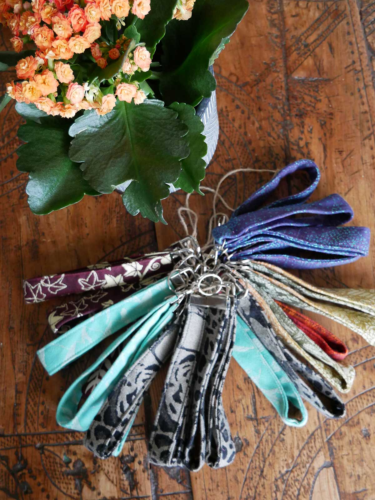 Collection of colorful fabric keychains on a wooden surface with flowers in the background