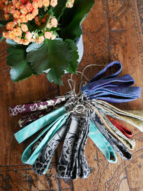Collection of colorful fabric keychains on a wooden surface with flowers in the background