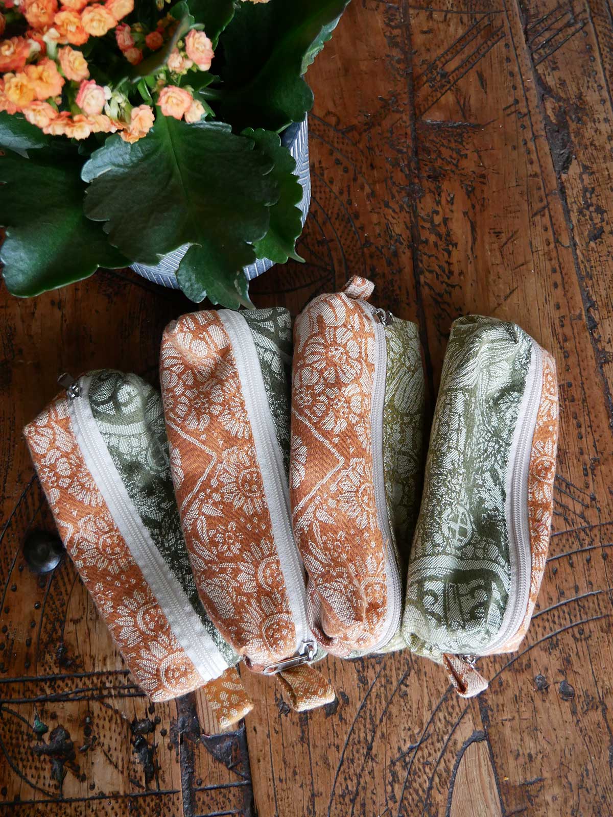 Four patterned pouches on a wooden surface with a plant in the corner.