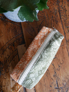 One zipped fabric pouche on a wooden surface with a plant in the corner.