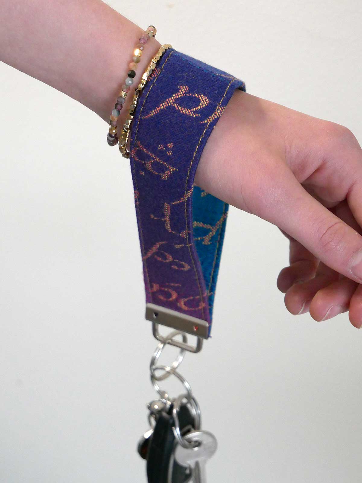 Hand wearing a purple fabric wristlet with keychain on a plain background