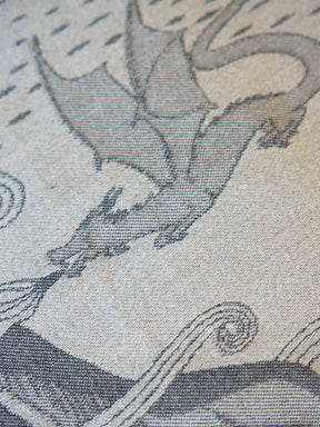 Close-up of a woven textile pattern featuring a gray dragon on a warm beige background.