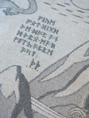 Close-up of a printed textile or fabric surface with gray line-art illustration and a cluster of dark gray characters on a light beige background.