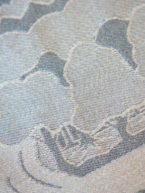 A close-up of a woven fabric with a cloud-like pattern in muted blue-gray and beige tones.