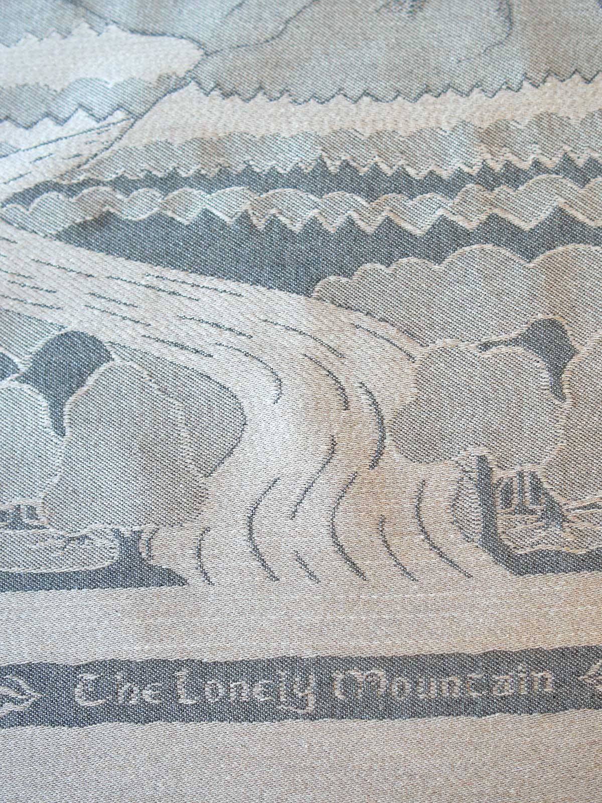Close-up of a woven textile depicting a mountain landscape with the text 'The Lonely Mountain' along the bottom.
