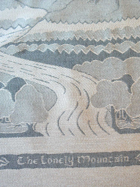 Close-up of a woven textile depicting a mountain landscape with the text 'The Lonely Mountain' along the bottom.