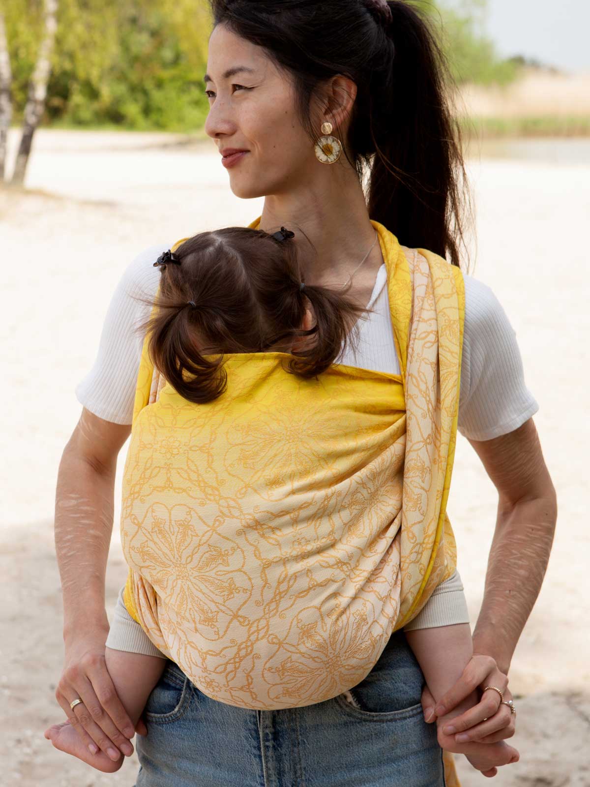 Model wearing lemon yellow baby wrap standing on a beach. 