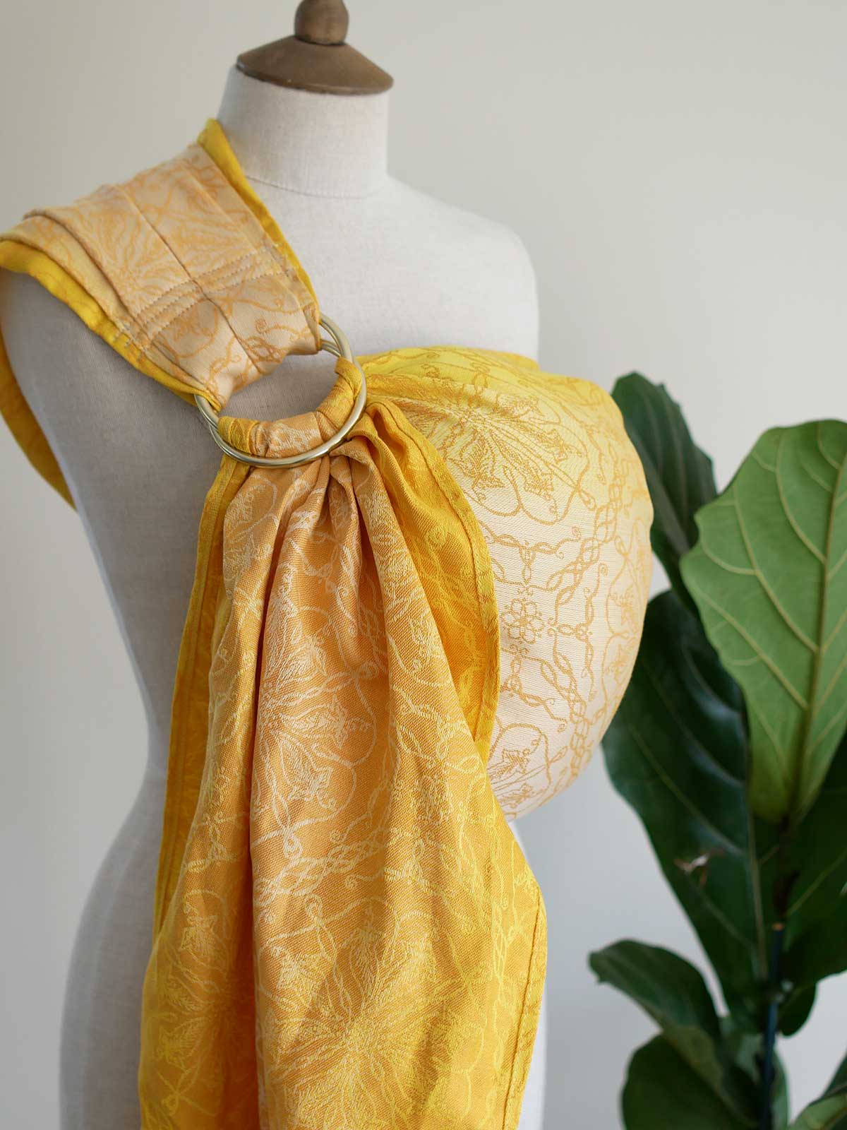 Side view of lemon yellow ring sling on mannequin with plant in background. 