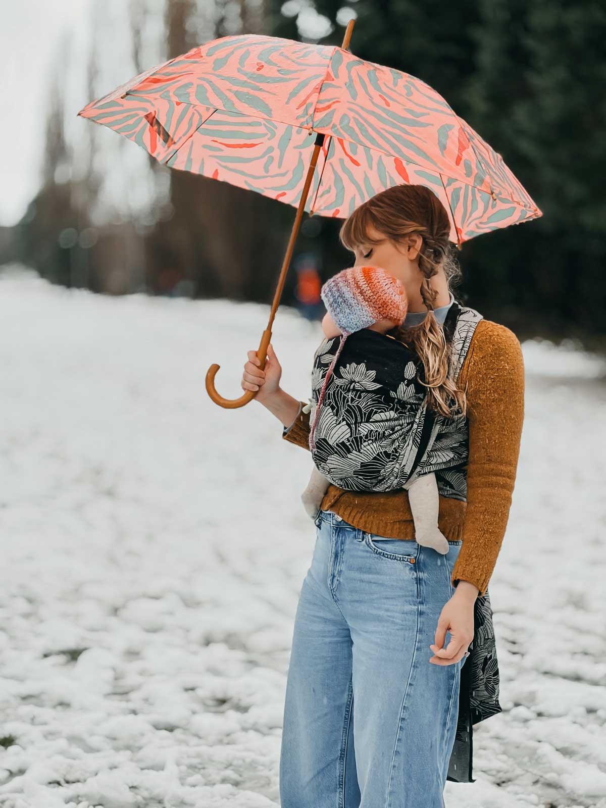 Person holding a patterned umbrella and carrying a baby in a snowy landscape