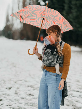 Person holding a patterned umbrella and carrying a baby in a snowy landscape