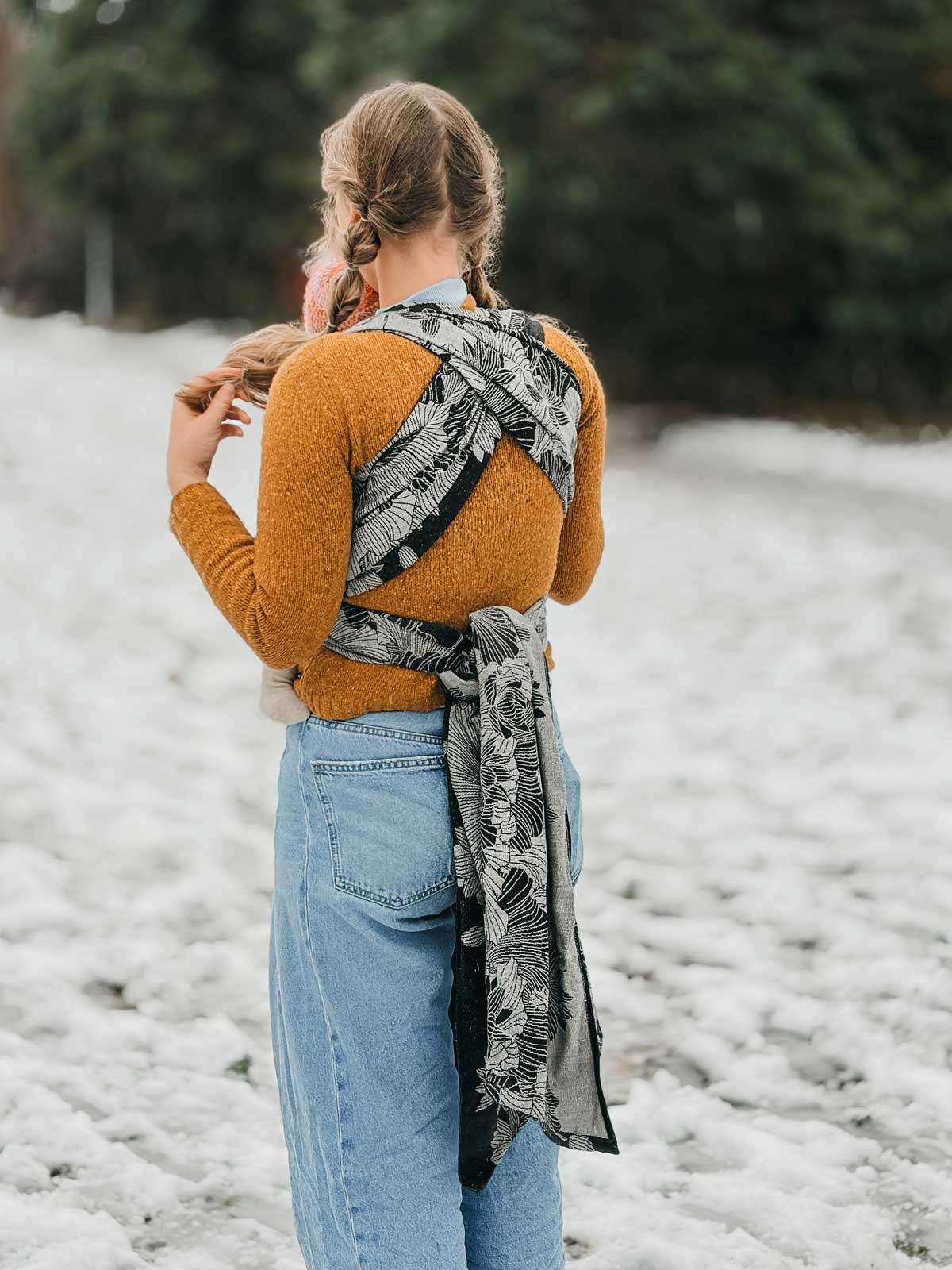 Person wearing a mustard sweater and blue jeans with a patterned scarf in a snowy landscape.