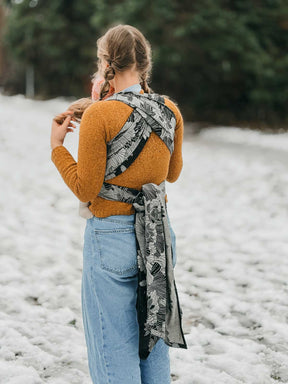 Person wearing a mustard sweater and blue jeans with a patterned scarf in a snowy landscape.