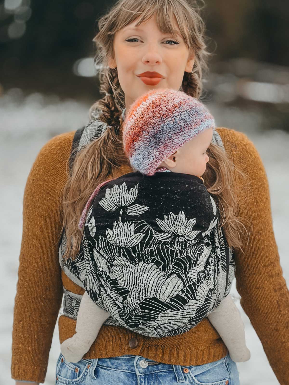 Woman carrying a baby in a floral baby carrier outdoors in winter.