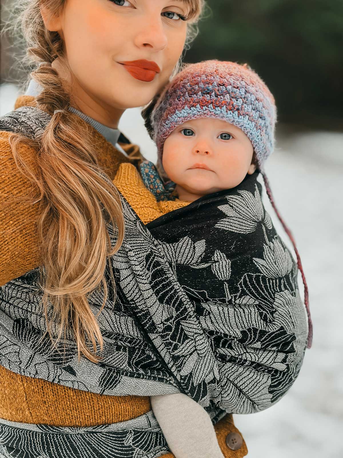 Woman holding a baby in a carrier outdoors in winter