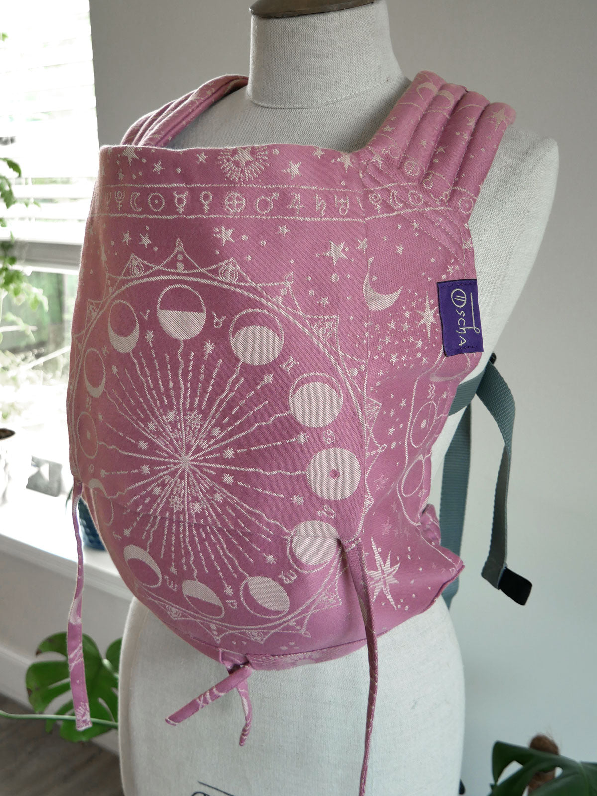 Pink baby carrier with celestial design on a mannequin against a white background