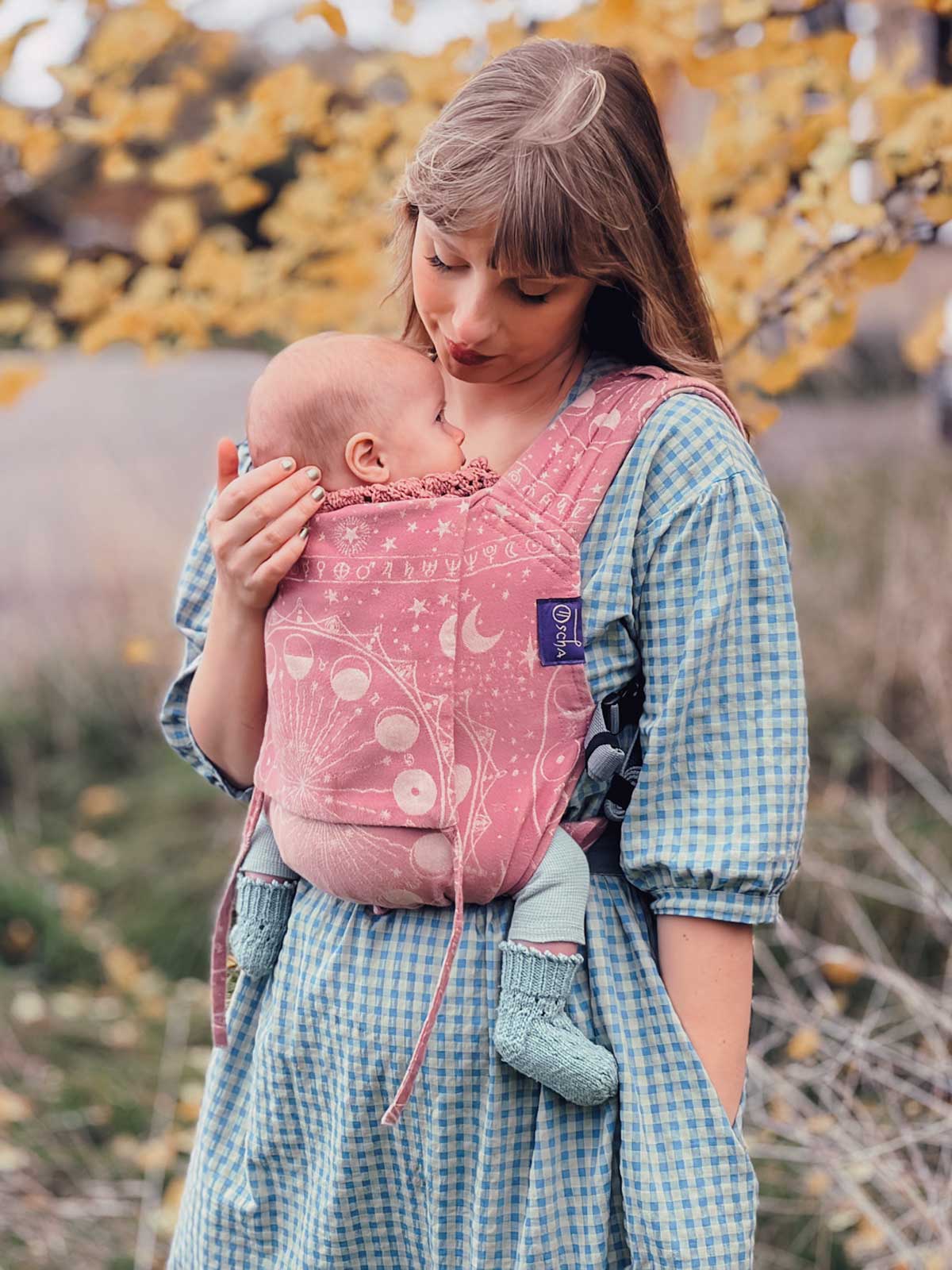 Model standing hands free using a dusky pink baby carrier. 