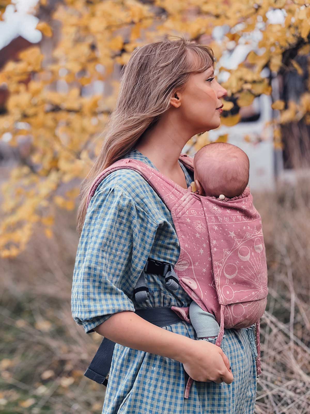 Side view of model carrying baby in a dusky pink Oscha carrier. 