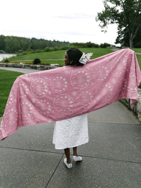 Person holding a pink patterned woven wrap outdoors on a path with greenery.