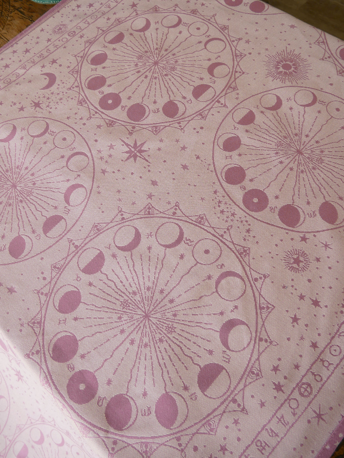 Pink fabric with celestial pattern featuring moons and stars on a wooden surface.