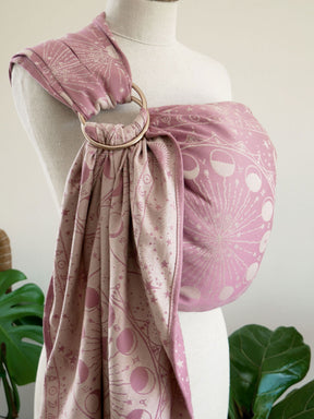 Mannequin wearing a pink ring sling, surrounded by green plants.
