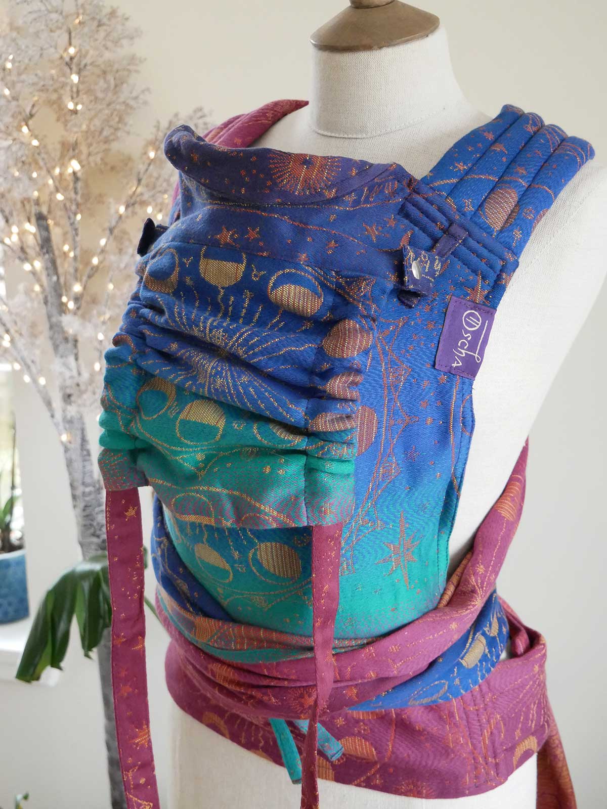 Colouful baby carrier on a mannequin with a decorated tree in the background